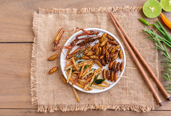 Mixed of crispy worm and insects in a ceramic bowl with chopsticks on a wood table. The concept of...