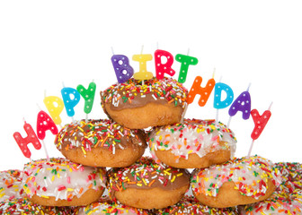 Chocolate and white frosted donuts covered in candy sprinkles piled into a cake pile isolated on white background with Happy Birthday candles.