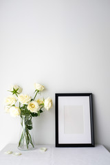 White roses in a glass vase on white table top on white background with copy space for product mockup placement for valentine's day wedding ceremony