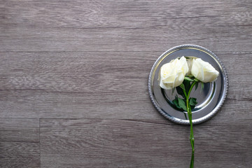 White roses on vintage round silver plate on wooden plank floor with copy space for valentine's day wedding ceremony