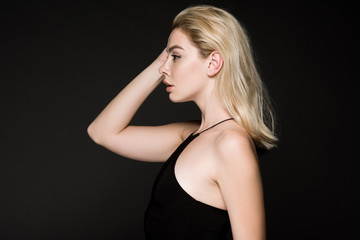Fototapeta na wymiar side view of blonde girl in black dress posing isolated on black