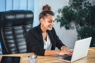 A young girl dressed in business clothes is working on a laptop.
