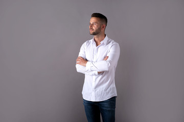 A serious handsome young man in a white shirt standing in front of a grey background in the studio.