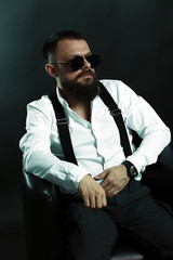 young handsome man with big beard and black sunglasses on black background  