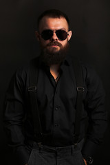 young handsome man with big beard and black sunglasses on black background  close up portrait 