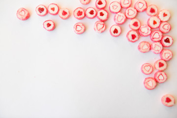 round red candy with a heart pattern lie on a white paper background as a texture and a corner frame