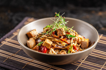 The concept of Japanese cuisine. Chinese noodles with chicken, grilled vegetables, and tofu in unagi sauce. Serving Asian dishes in the restaurant in a plate on a bamboo mat. Top view, copy space