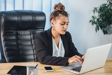 A young girl dressed in business clothes is working on a laptop.