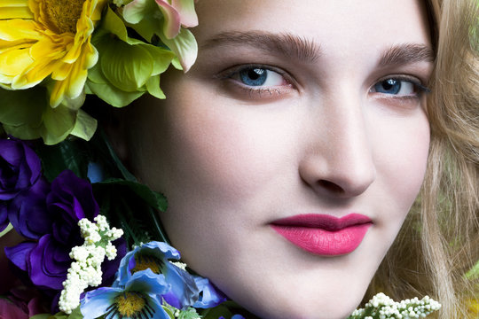 Young woman's face with red lipstick surrounded by colorful flowers, close up.