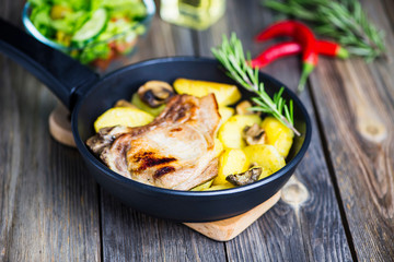 grilled pork steak with bone with potatoes and mushrooms in a frying pan on a wooden board