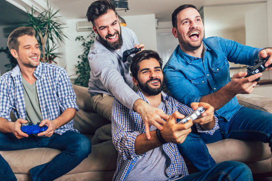 Smiling male friends playing video games at home and having fun.
