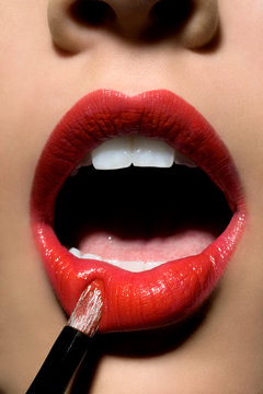 Closeup of female lips with red lipstick and makeup brush.