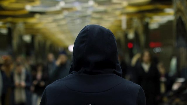 Rear view of a man with a dark blue hoodie on standing in front of a crowd at the station, resistance concept. Close up for man back in front of many people in subway.