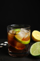 Glass of cocktail with cola, ice and cut lime on table against black background. Space for text