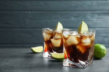 Glasses of cocktail with cola, ice and cut lime on table. Space for text