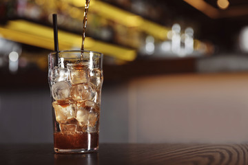 Pouring cola into glass with ice cubes on table indoors. Space for text