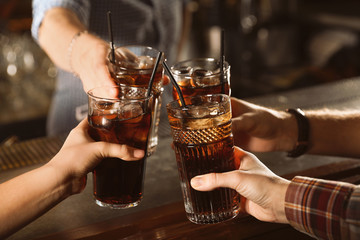 Group of friends clinking glasses with cola at table indoors, closeup