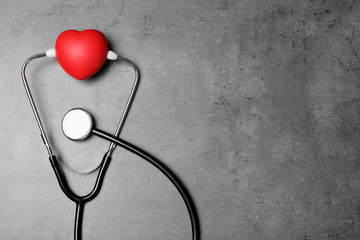 Stethoscope and red heart with space for text on grey background, top view