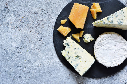 A Set Of Cheeses: Brie, Blue Cheese, Parmesan, Camembert On A Slate Board. Plate With Delicacies. View From Above