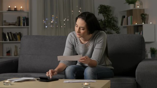 Single sad woman accounting checking receipts sitting on a couch in the night at home