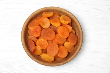 Wooden bowl with dried apricots on white table, top view. Healthy fruit
