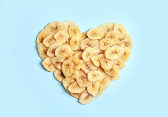 Heart shaped heap of sweet banana slices on color background, top view. Dried fruit as healthy snack