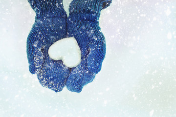 Female hands in knitted mittens with heart of snow in winter day. Love concept. Valentine day background.