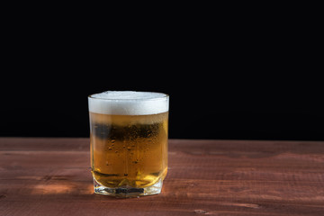 light beer with foam in a glass on a wooden table