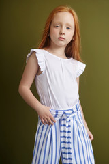 Beautiful red-haired girl with long hair and beautiful big blue eyes. Redhead Girl child in summer clothes posing on the background of olive color. Norwegian girl with bright red hair