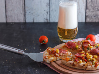 Pizza with corn, sausage, tomatoes on a wooden board and light beer with foam in a glass