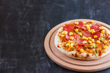 Pizza with corn, sausage, tomatoes on a wooden round board