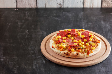 Pizza with corn, sausage, tomatoes on a wooden round board