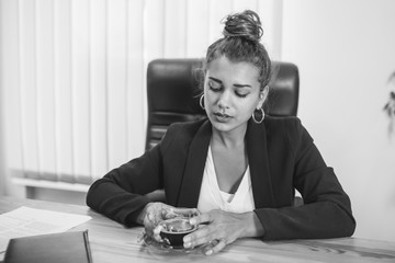 Young business girl in the office wondering. During this time she enjoys a black, fragrant coffee.