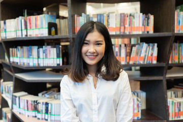 Happy young woman in the library with books to search information.