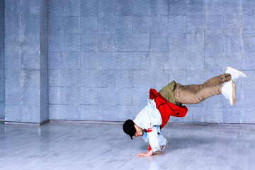 Young man standing on hands in dance. Fashion style dancer raised his leg standing on hands on grey...
