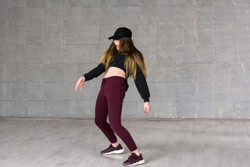 Modern style dancer is dancing. Young girl dancer posing on grey background. Young female dancer practicing dance element.