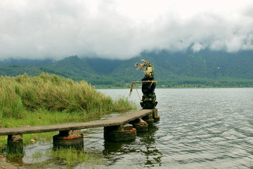 Place of prayer and power. Bratan lake in fog. Traditional balinese ritual offerings in straw baskets for Hindu spirits and gods with flowers and aromatic sticks