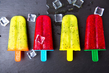 Homemade popsicle with lime juice, kiwi fruit and raspberry against black stone background.