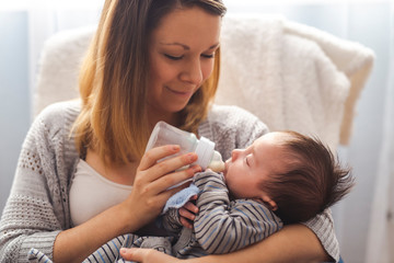 Portrait of a pretty mother feeding her newborn baby from a bottle while relaxing at home