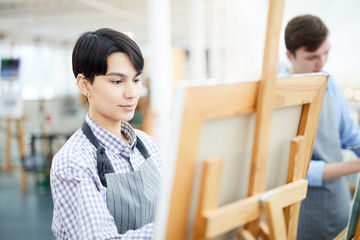 Portrait of female art student painting picture on easel enjoying work in studio, copy space