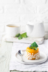 Piece of mango mousse cake on plate over white wooden table.