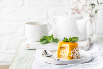 Piece of mango mousse cake on plate over white wooden table.