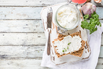 Crispbread toast with homemade herb and garlic cottage cheese on wooden background, top view