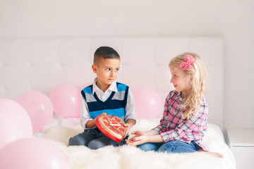 Obraz na płótnie Canvas Group portrait of two Caucasian cute adorable children eating heart shaped candies. Boy giving girl chocolate gift present to celebrate Valentine Day. Love and friendship concept. Best friends forever