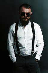 young handsome man with big beard and black sunglasses on black background  