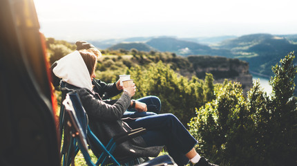 love couple sit in camping chairs on top of sun flare mountain, travelers drink tea on cup enjoy...