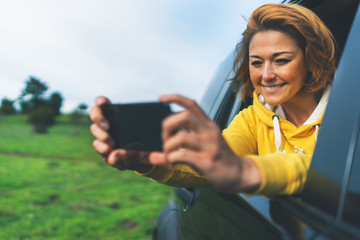 smile tourist girl in an open window of a auto car taking photo selfie on mobile smart phone, person looking on camera gadget technology, blogger using content online wifi internet concept