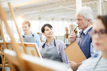 Portrait of smiling art student looking at teacher during class in workshop studio, copy space