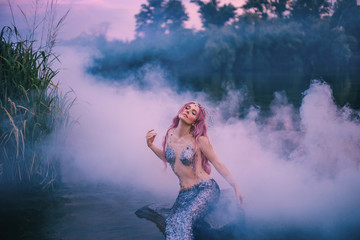 Obraz na płótnie Canvas mysterious mythical creature enjoys wind and fresh air in forest lake, sea maiden feeds on morning sun in a thick pink mist, mermaid with pink hair waiting for bright rays to become human