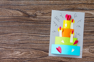 Greeting card with birthday cake congratulation on a wooden table. Children's art project craft for...